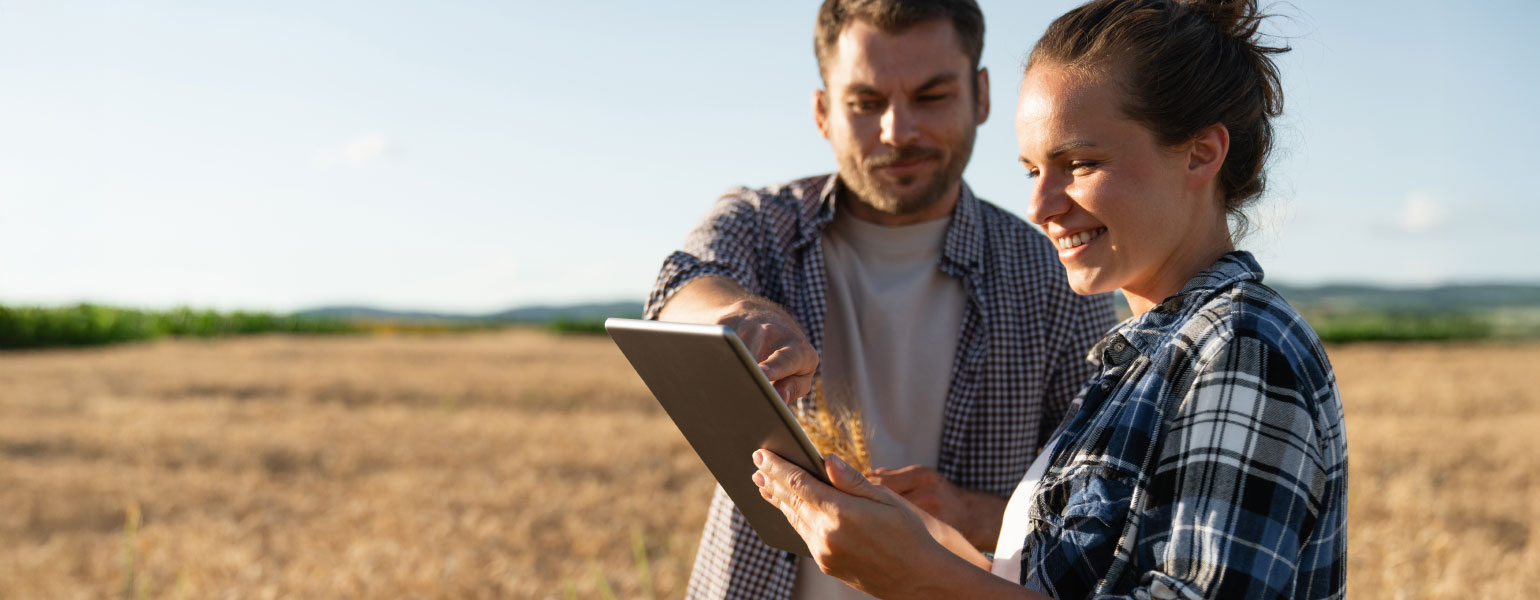 Man and woman standing in field looking at tablet